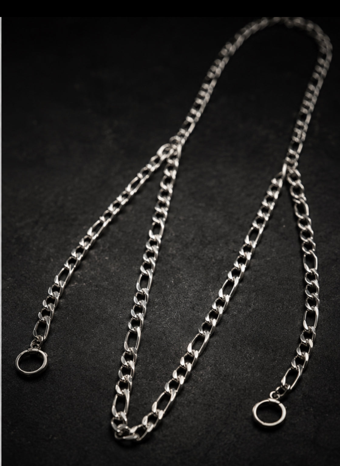 A silver ARKS Figaro chain laid out at full length, its two clasps open and no earplugs attached.