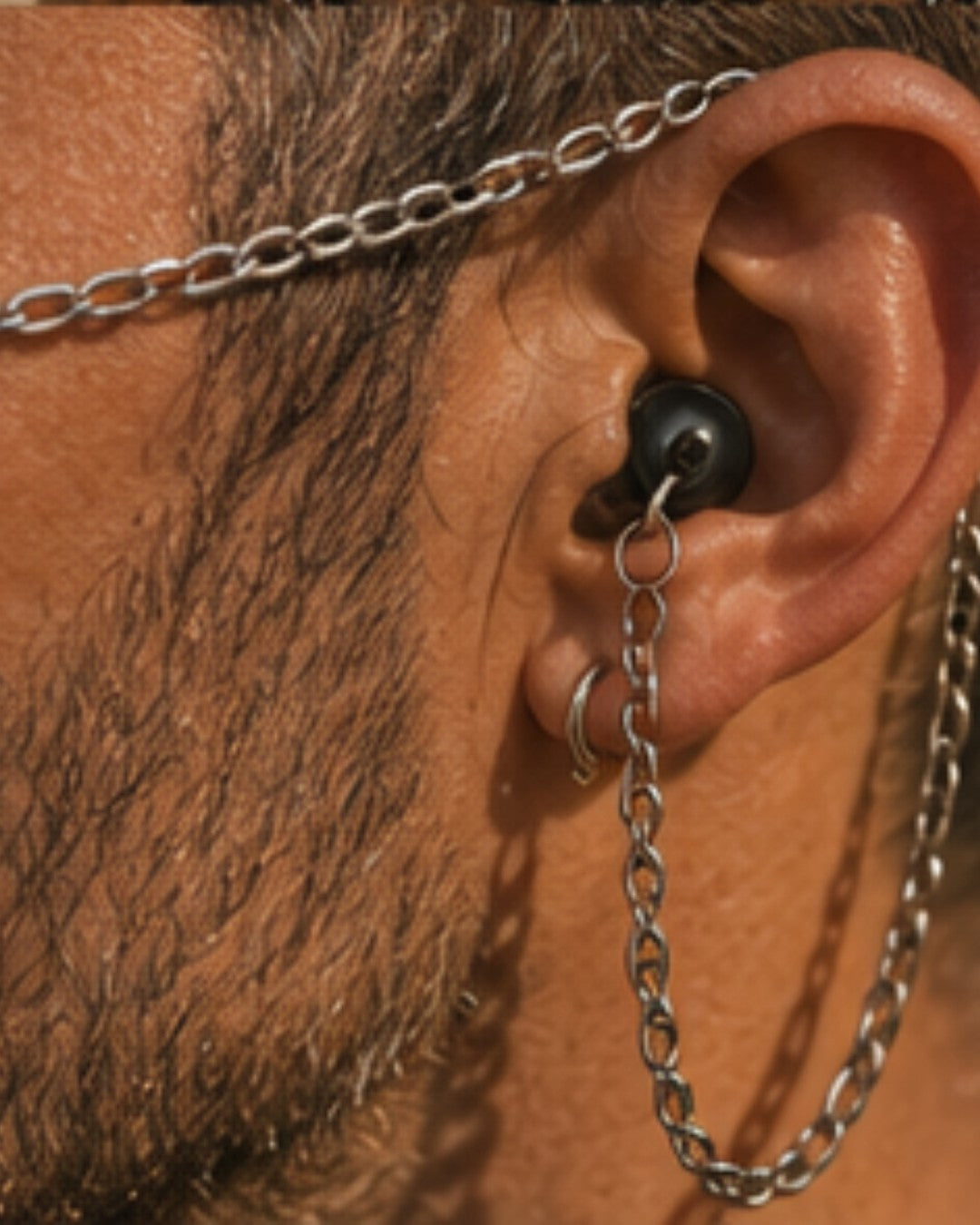 Close up of an ARKS earplug worn in the ear with the chain hanging from it.