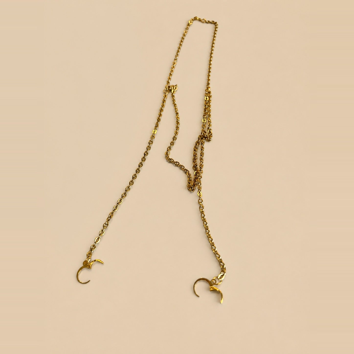 A gold ARKS chain laid out at full length, its two clasps open and no earplugs attached.