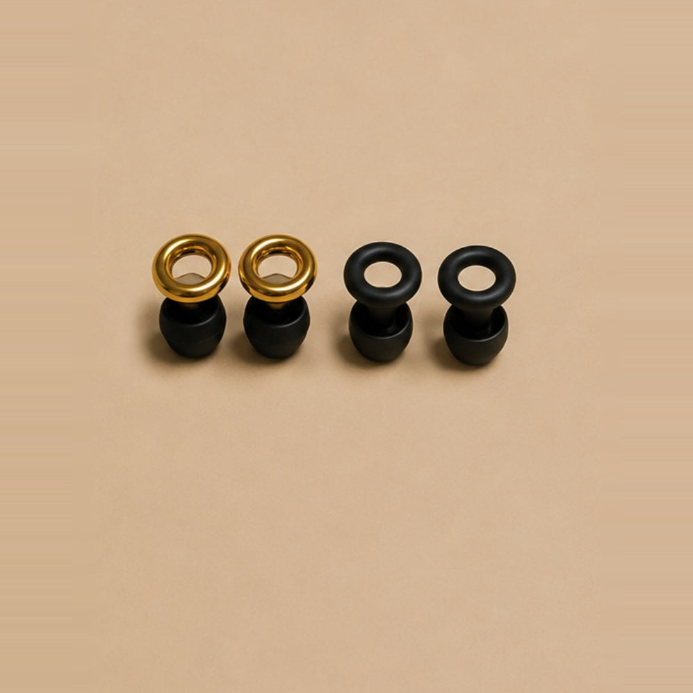 Four matte black ARKS earplugs, two with gold rings and two with black rings.